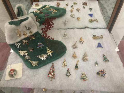 A display of broach-style pins that look like Christmas trees. They are lying on white felt and a green stocking.